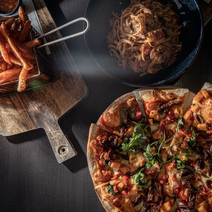 Delicious gourmet pizza, pasta, and sweet potato fries on a stylish table setting. Perfect for food lovers.