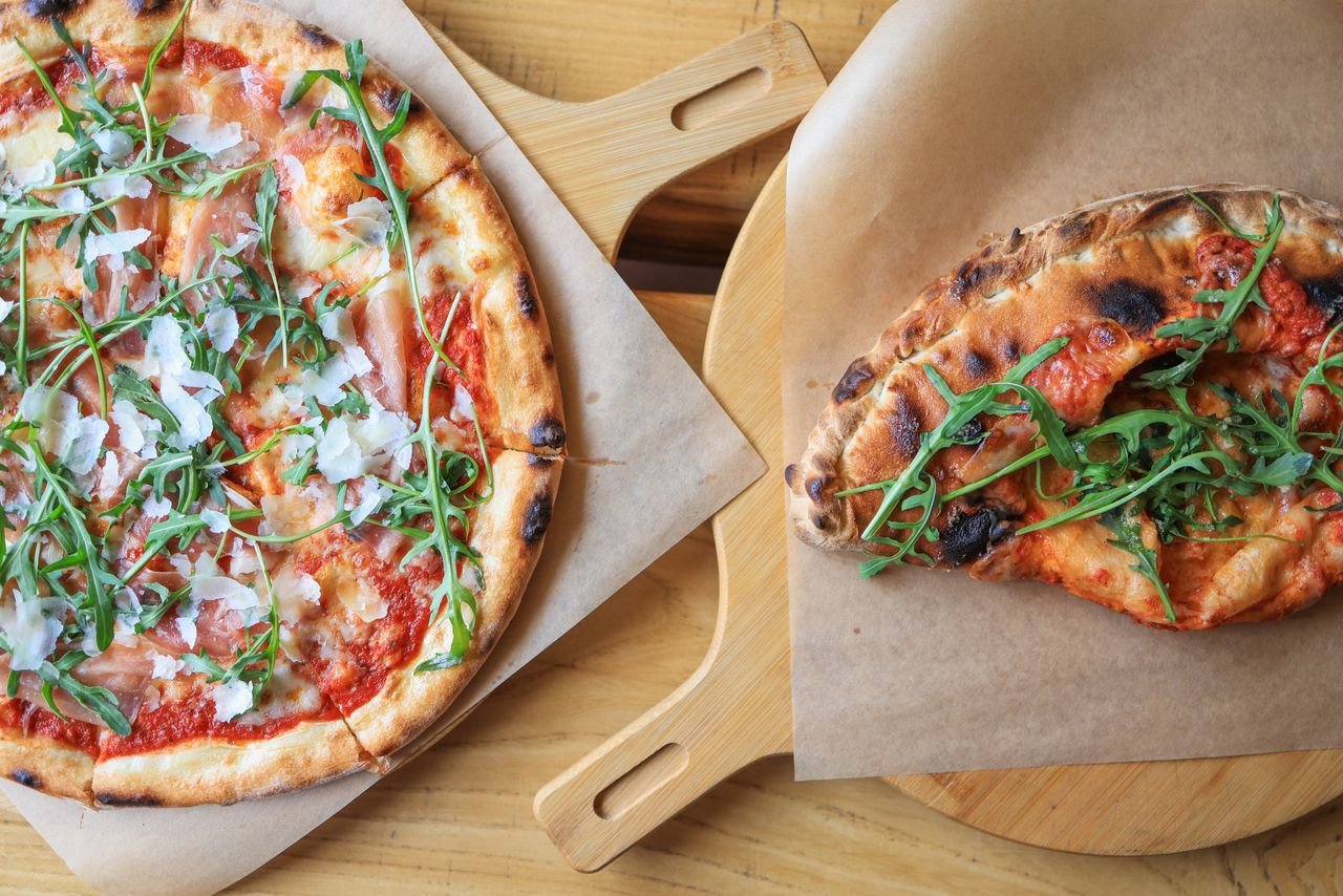 Freshly baked pizzas topped with prosciutto, arugula, and cheese, served on wooden boards.