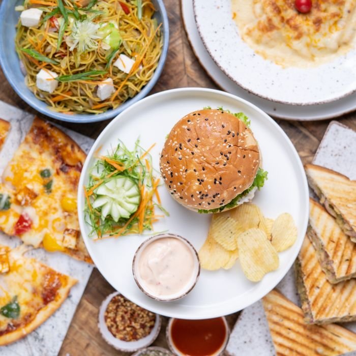 Top view of a diverse meal spread including a burger, noodles, pizza, and more on a wooden table.