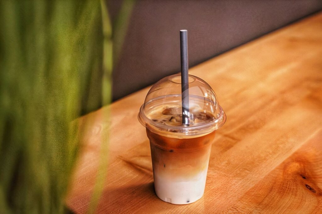 A refreshing iced coffee in a plastic cup with a straw, on a wooden table.