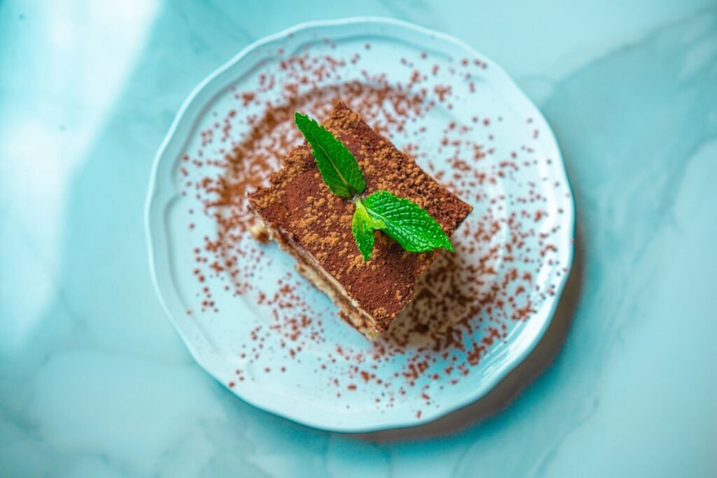 Indulge in a slice of tiramisu garnished with fresh mint on a classic marble plate.