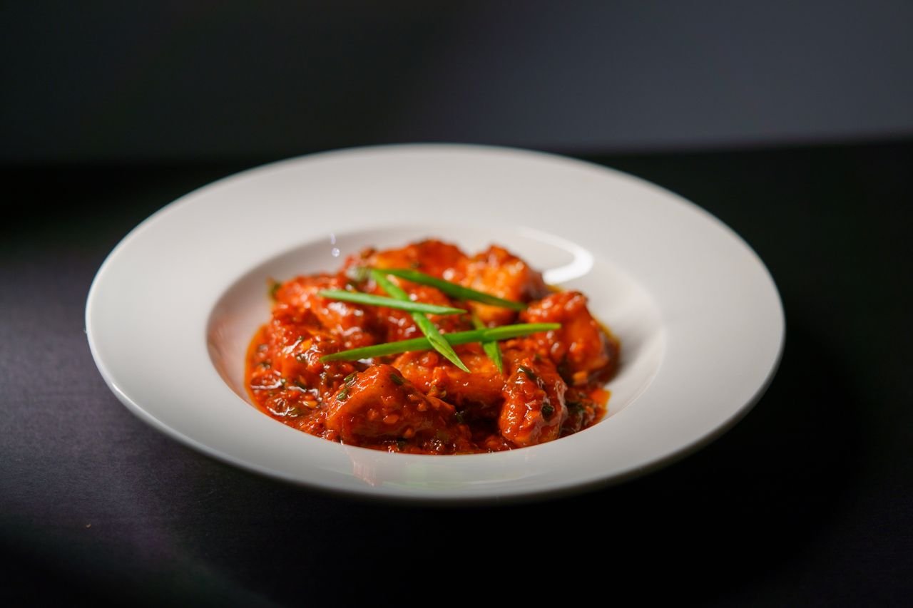 Spicy Indian paneer tikka served in a rich tomato-based gravy, garnished with green scallions.