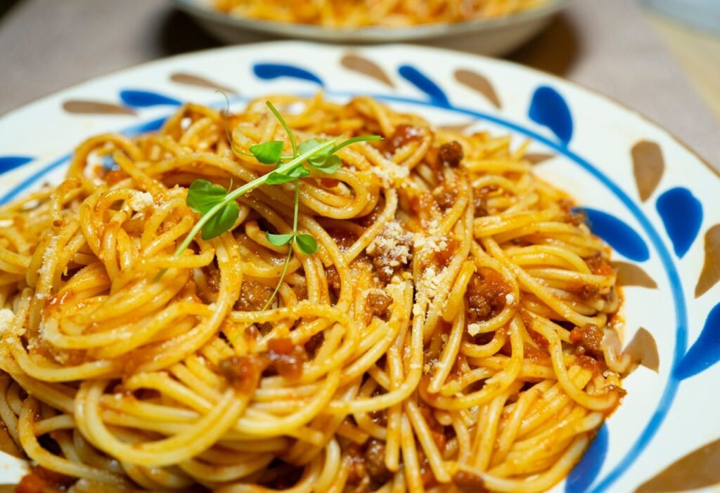 Close-up of savory spaghetti Bolognese garnished with fresh herbs on a decorative plate.