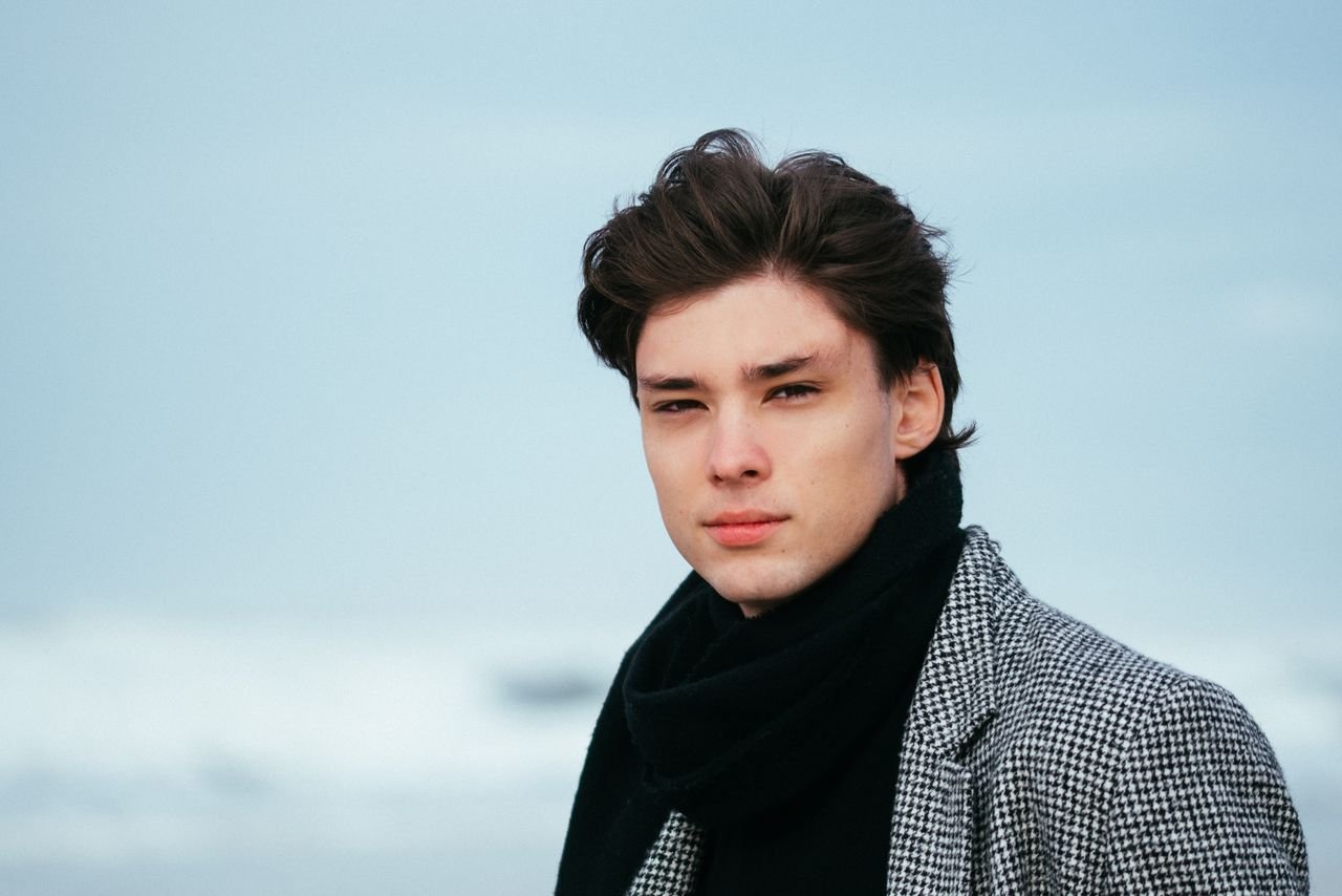 Young man in winter fashion standing at the beach with a calm expression.