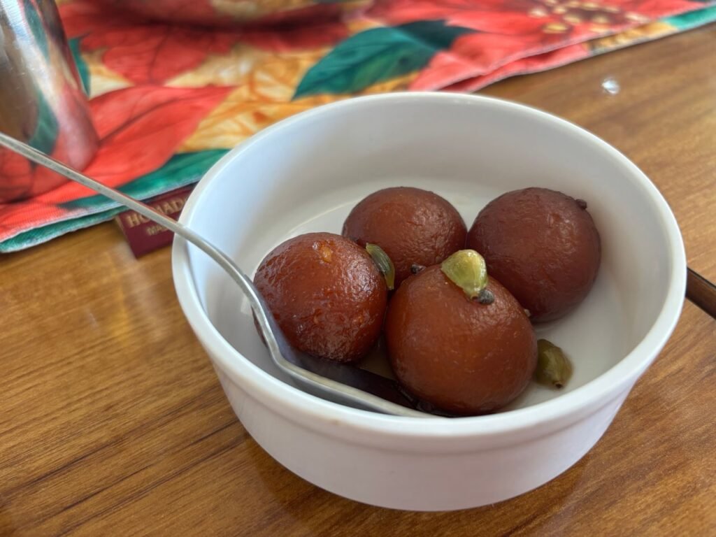 Close-up of gulab jamun, a sweet Indian dessert, served in a white bowl with a spoon.