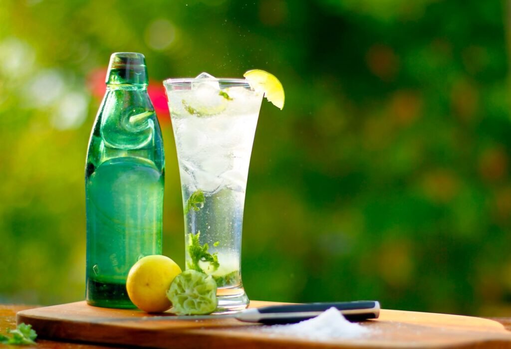 A tall glass of lime soda with ice and citrus fruits on a sunny day.