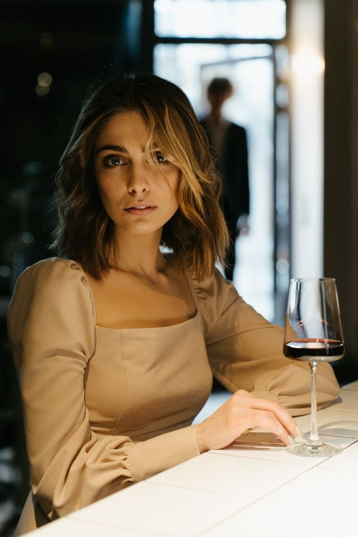 A woman in an elegant dress enjoys wine at a stylish indoor bar setting.