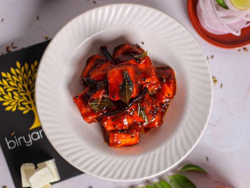 Delicious spicy paneer curry served with fresh curry leaves, top view on a white plate.